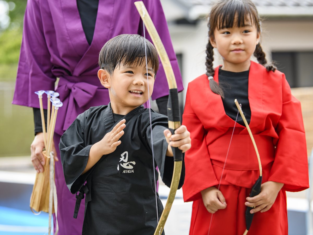 弓矢体験に挑戦する赤と黒の忍者衣装の子どもたち