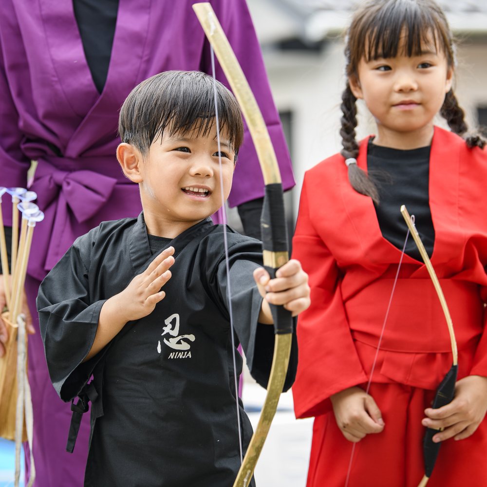 弓矢体験に挑戦する赤と黒の忍者衣装の子どもたち
